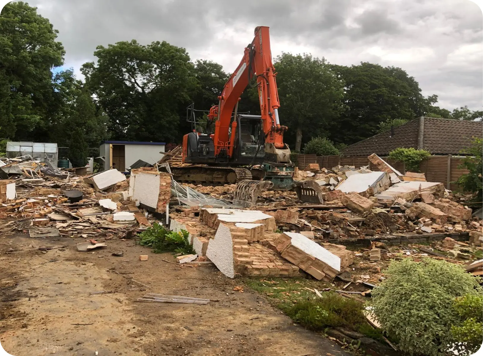 Orange excavator demolishing a structure among brick rubble